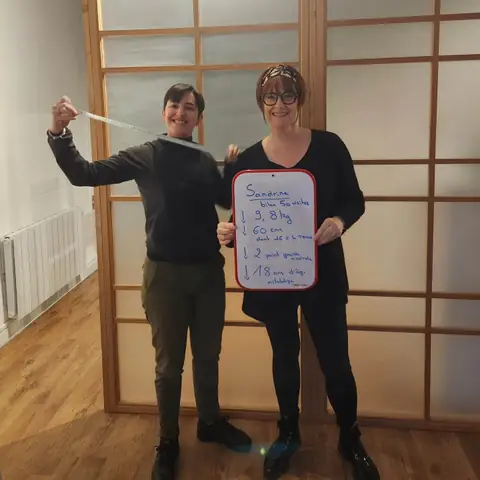 Dans la salle du club, une membre sourit et présente son bilan inscrit sur l’ardoise