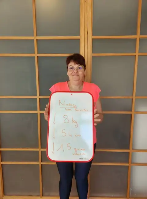 Dans la salle du club, une membre sourit et présente son bilan inscrit sur l’ardoise
